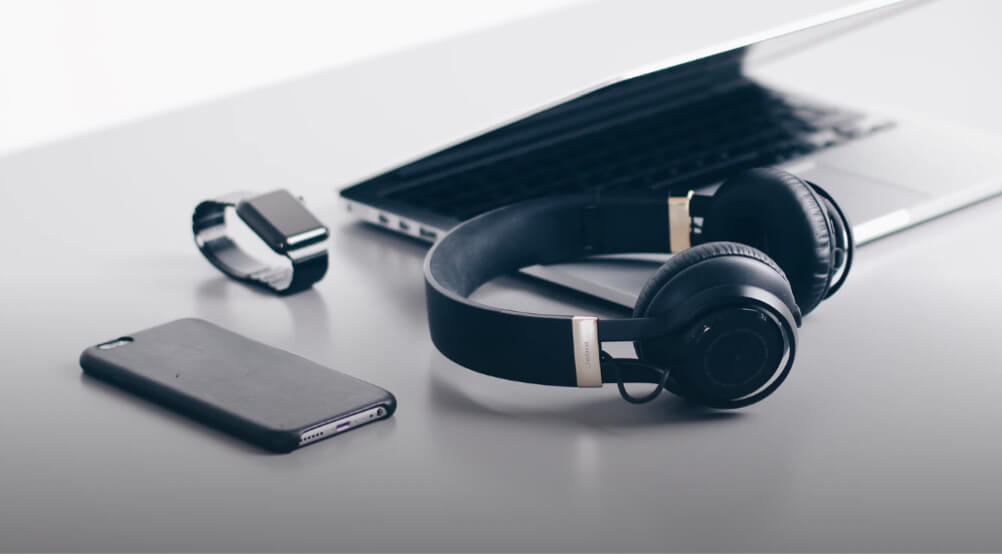 Headphones, an iPhone, an Apple Watch, and a MacBook Pro sitting on a silver table